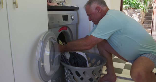 Caucasian senior man putting clothes in washing machine at home. staying at home in self isolation in quarantine lockdown
