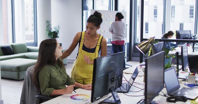 Two diverse female work colleagues looking at computer monitor and talking. working at the office of an independent creative business