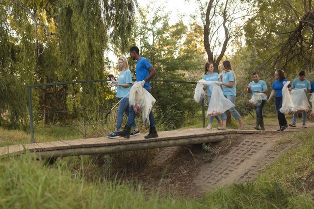Multi ethnic group of conservation volunteers cleaning up river in the countryside, walking over bridge holding rubbish bags. Ecology and social responsibility in rural environment.