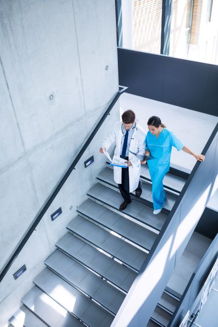 Doctor and nurse discussing over a report while climbing down stairs - Download Free Stock Photos Pikwizard.com