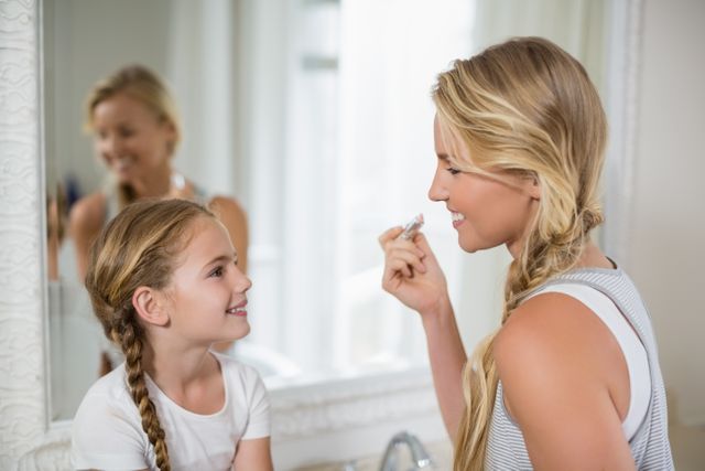 Mother interacting with daughter while applying a lipstick in bathroom - Download Free Stock Photos Pikwizard.com