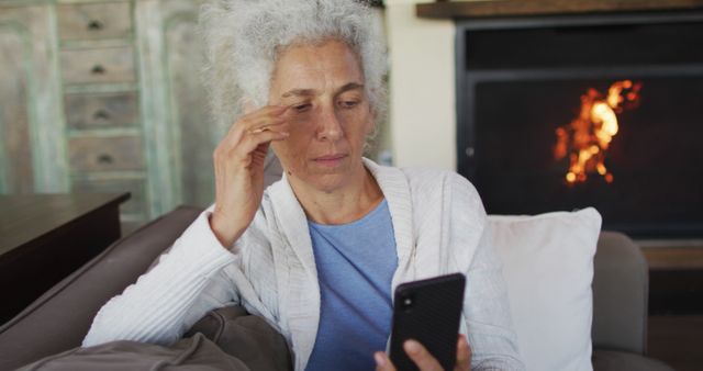 Senior mixed race woman sitting on sofa using smartphone. retirement and senior lifestyle, spending time alone at home.