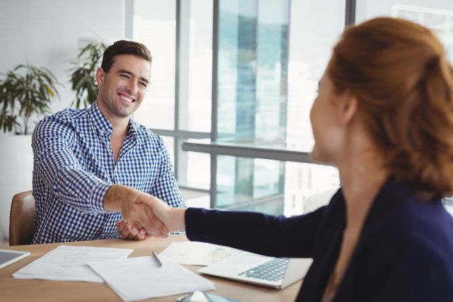 Smiling executives shaking hands at desk in office
