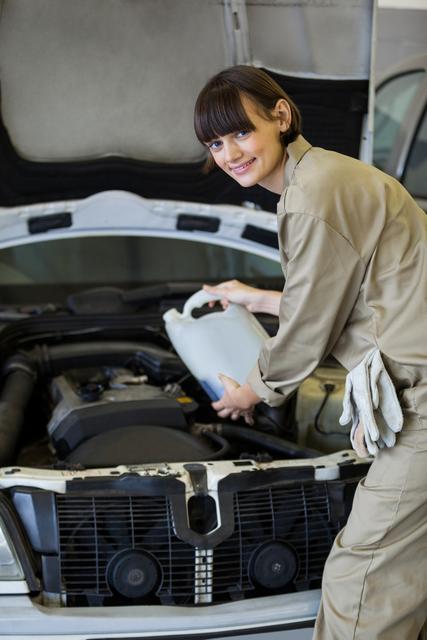 Female mechanic pouring oil lubricant into the car engine at the garage