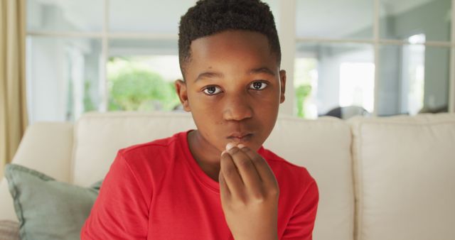 Portrait of sad african american boy sitting in living room gesturing with hand to mouth - Download Free Stock Photos Pikwizard.com