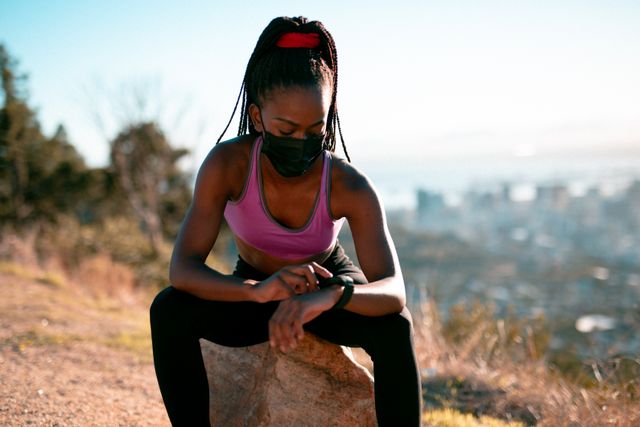 Fit african american woman wearing face mask, resting, checking smartwatch in countryside - Download Free Stock Photos Pikwizard.com