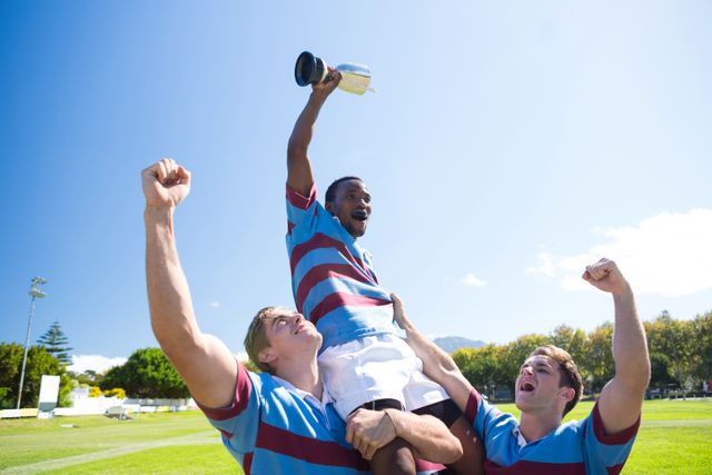 Happy rugby team enjoying victory while standing at field against sky on sunny day