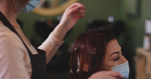 Causian female hairdresser and client in face masks, hair being dyeing ...