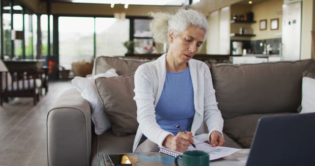 Senior mixed race woman sitting on sofa taking notes. retirement and senior lifestyle, spending time alone at home.