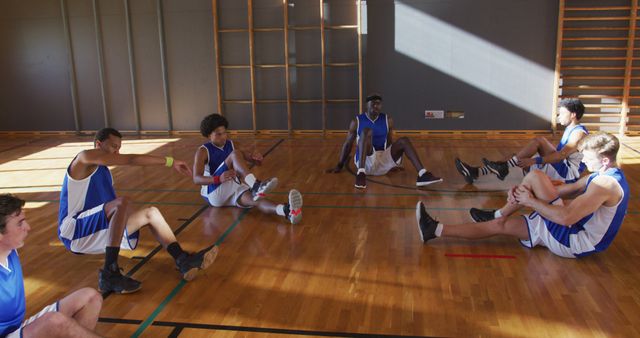 Diverse male basketball team wearing blue sportswear and stretching. basketball, sports training at an indoor court.