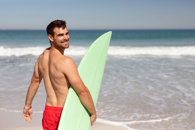 Shirtless man with surfboard looking at camera on beach in the sunshine - Download Free Stock Photos Pikwizard.com