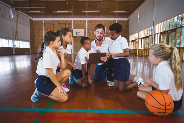 Sport teacher and school kids discussing on clipboard in basketball court - Download Free Stock Photos Pikwizard.com