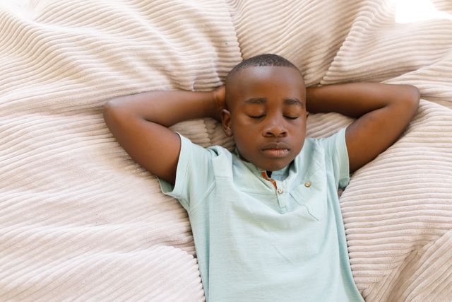 Close up of an african american boy lying in bed with eyes closed and arms behind his head - Download Free Stock Photos Pikwizard.com
