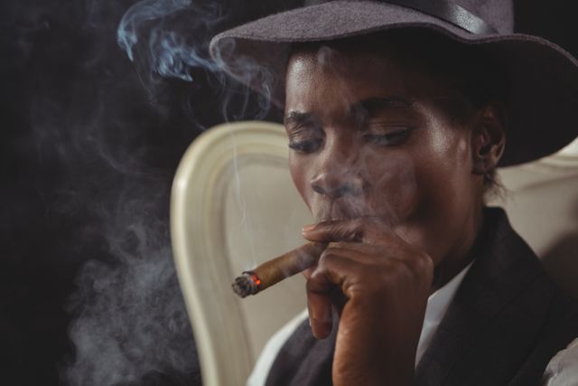 Androgynous man smoking cigar while sitting on a chair - Download Free Stock Photos Pikwizard.com