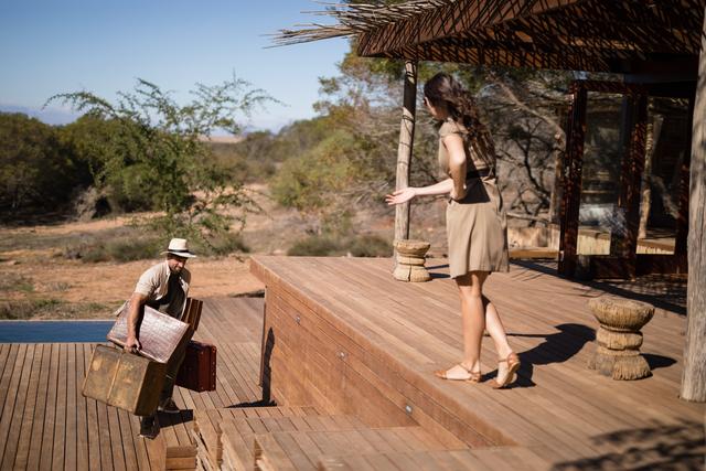 Woman gesturing while man carrying a suitcase during safari vacation