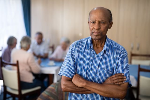 Portrait of senior man standing with arms crossed against friends at nursing home
