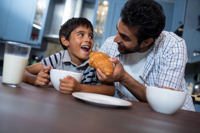 Smiling father feeding croissant to son - Download Free Stock Photos Pikwizard.com