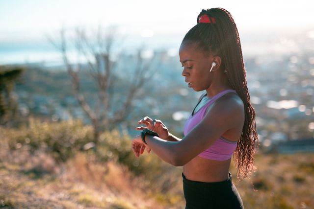 Fit african american woman exercising in countryside, wearing earphones and checking smartwatch - Download Free Stock Photos Pikwizard.com
