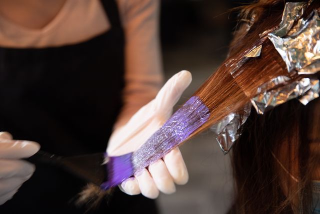 Caucasian female hairdresser working in hair salon wearing colouring hair of female customer wearing gloves. Health and hygiene in workplace during Coronavirus Covid 19 pandemic.