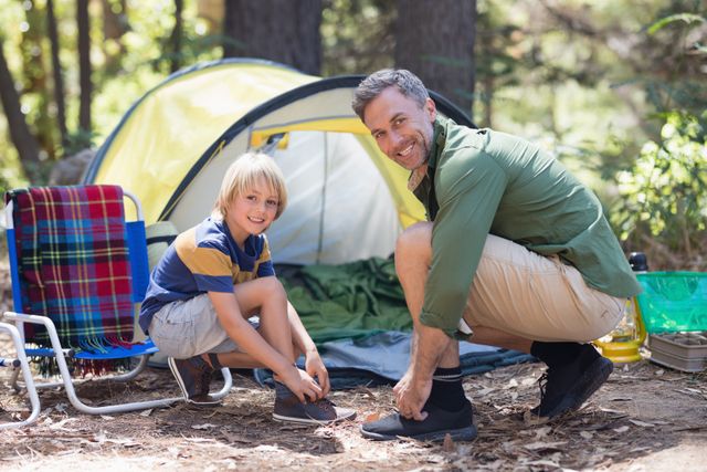Portrait of smiling father and son tying shoelace by tent at campsite