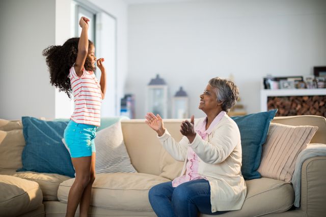 Grandmother applauding her granddaughter while dancing in living room - Download Free Stock Photos Pikwizard.com