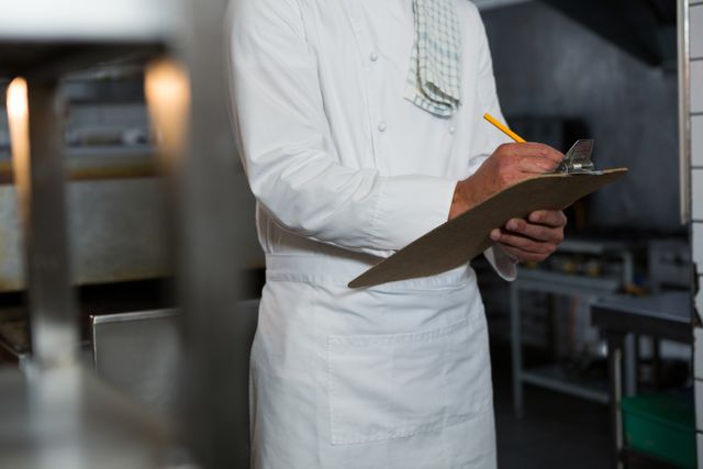 Mid-section of male chef writing order on a clipboard