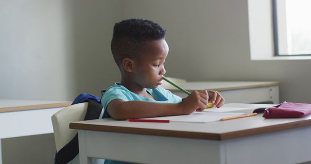 Image of african american boy sitting at desk during lesson in classroom. primary school education and learning concept.