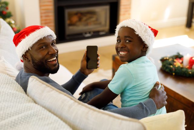 Rearview of an african-american man and his son wearing santa hats sitting on the couch looking behi - Download Free Stock Photos Pikwizard.com