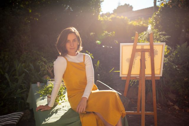 Caucasian woman posing in garden with canvas and easel - Download Free Stock Photos Pikwizard.com