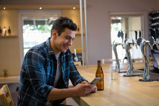 Smiling young man using phone at counter in restaurant