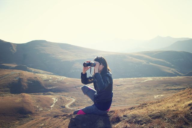 Woman Wearing Black Jacket Using Binoculars Sitting on Mountain - Download Free Stock Photos Pikwizard.com