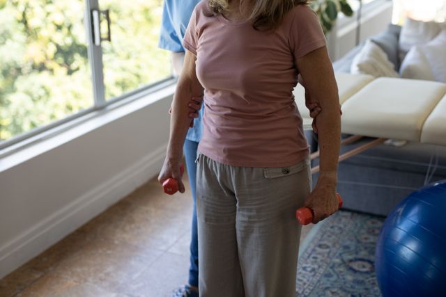 Mid section of female health worker assisting senior woman to exercise with dumbbells at home - Download Free Stock Photos Pikwizard.com