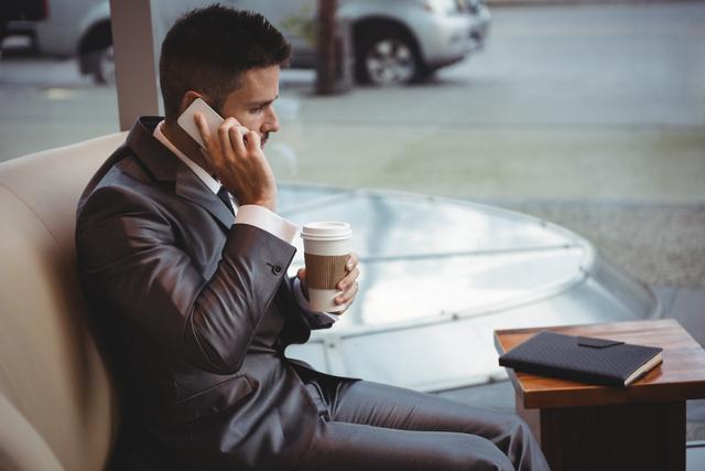 Businessman holding coffee while talking on mobile phone - Download Free Stock Photos Pikwizard.com