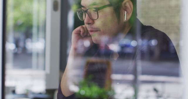 Asian man wearing wireless earphones having a image call on laptop while sitting at a cafe. business and lifestyle concept