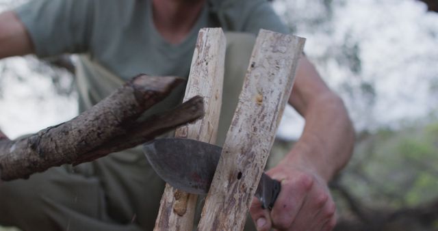 Caucasian male survivalist using branch and machete to cleave firewood at camp in wilderness. exploration, travel and adventure, survivalist in nature.