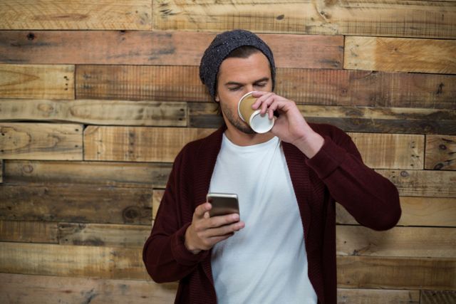 Man using mobile phone while having a coffee against wooden wall - Download Free Stock Photos Pikwizard.com