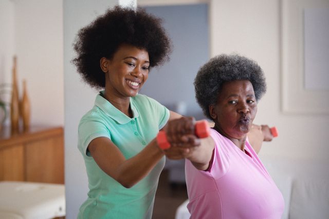 African american female physiotherapist helping senior woman to exercise with dumbbells at home - Download Free Stock Photos Pikwizard.com