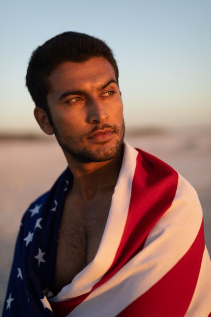 Young man wrapped in American flag standing on the beach