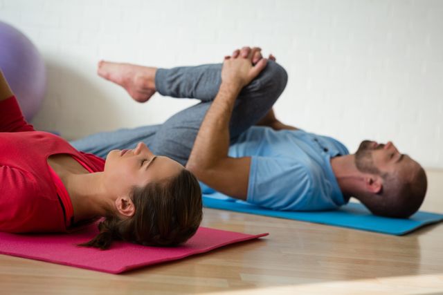 Instructor and student exercising while lying on mat in yoga studio - Download Free Stock Photos Pikwizard.com