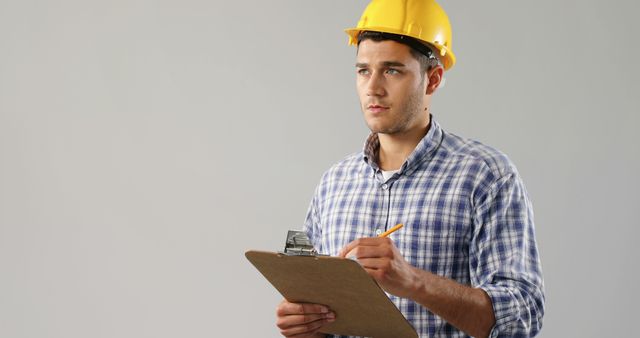 A young Caucasian man wearing a hard hat holds a clipboard, with copy space - Download Free Stock Photos Pikwizard.com
