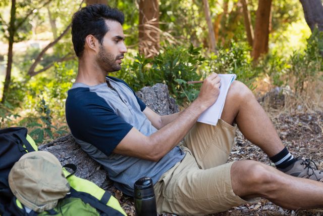 Man writing on notepad while resting on tree trunk - Download Free Stock Photos Pikwizard.com