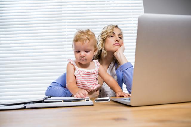 Stressed mother with baby girl using laptop - Download Free Stock Photos Pikwizard.com
