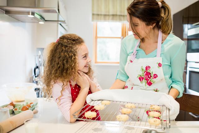 Mother interacting with daughter while holding cookies in cooling rack at kitchen