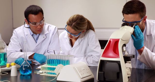 Three focused diverse scientists working, using microscope, wearing ...