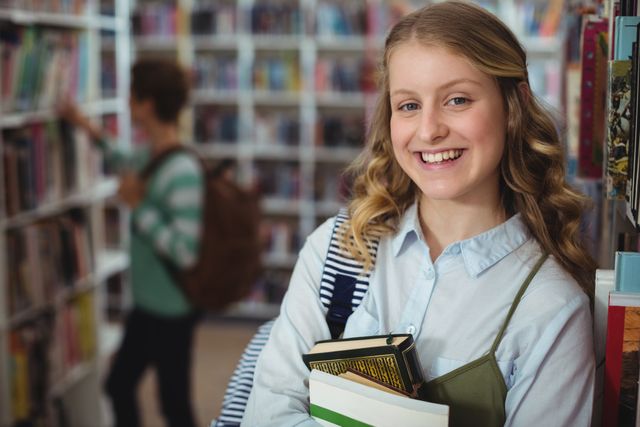 Portrait of happy schoolgirl holding books in library - Download Free Stock Photos Pikwizard.com