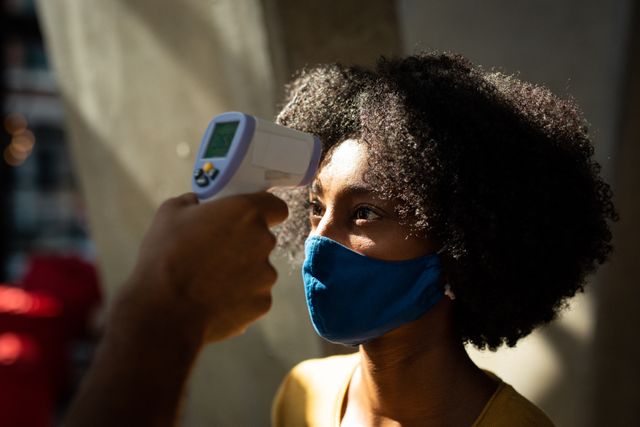 African american woman wearing face mask having temperature taken by colleague before work - Download Free Stock Photos Pikwizard.com