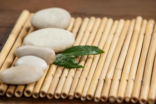 Two green leaves and four white stones on the bamboo mat- Download Free Stock Photos Pikwizard.com
