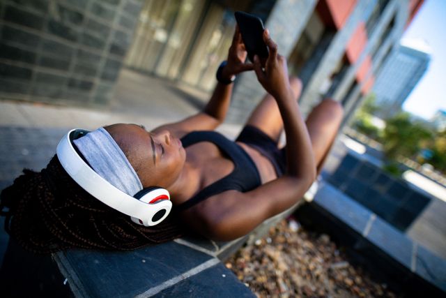Fit african american woman wearing headphones, resting, using smartphone in street - Download Free Stock Photos Pikwizard.com