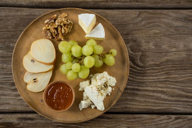 Cheese with grapes, apple slices, walnuts and sauce on wooden plate - Download Free Stock Photos Pikwizard.com