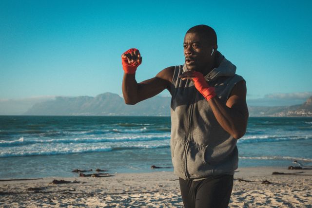 African american man exercising, shadowboxing with wrapped hands on beach at sunset - Download Free Stock Photos Pikwizard.com